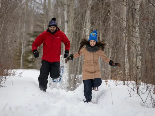 Two People running down a trail in snowshoes.