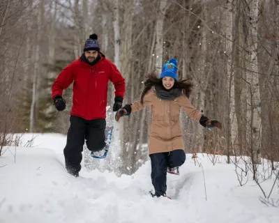 Two People running down a trail in snowshoes.